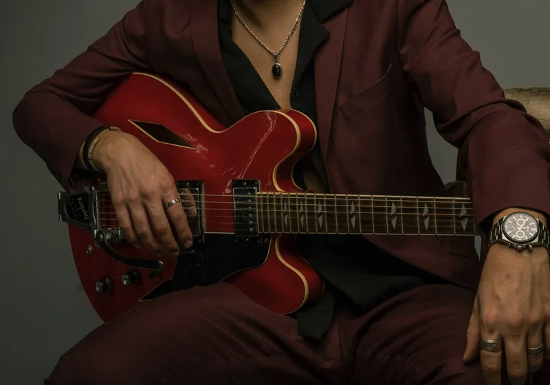 Zeegwon Shilling's hands on his red Gibson guitar, in a burgundy suit