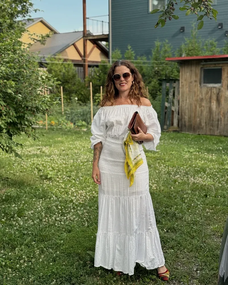 iskwē standing in a summer garden in a white dress